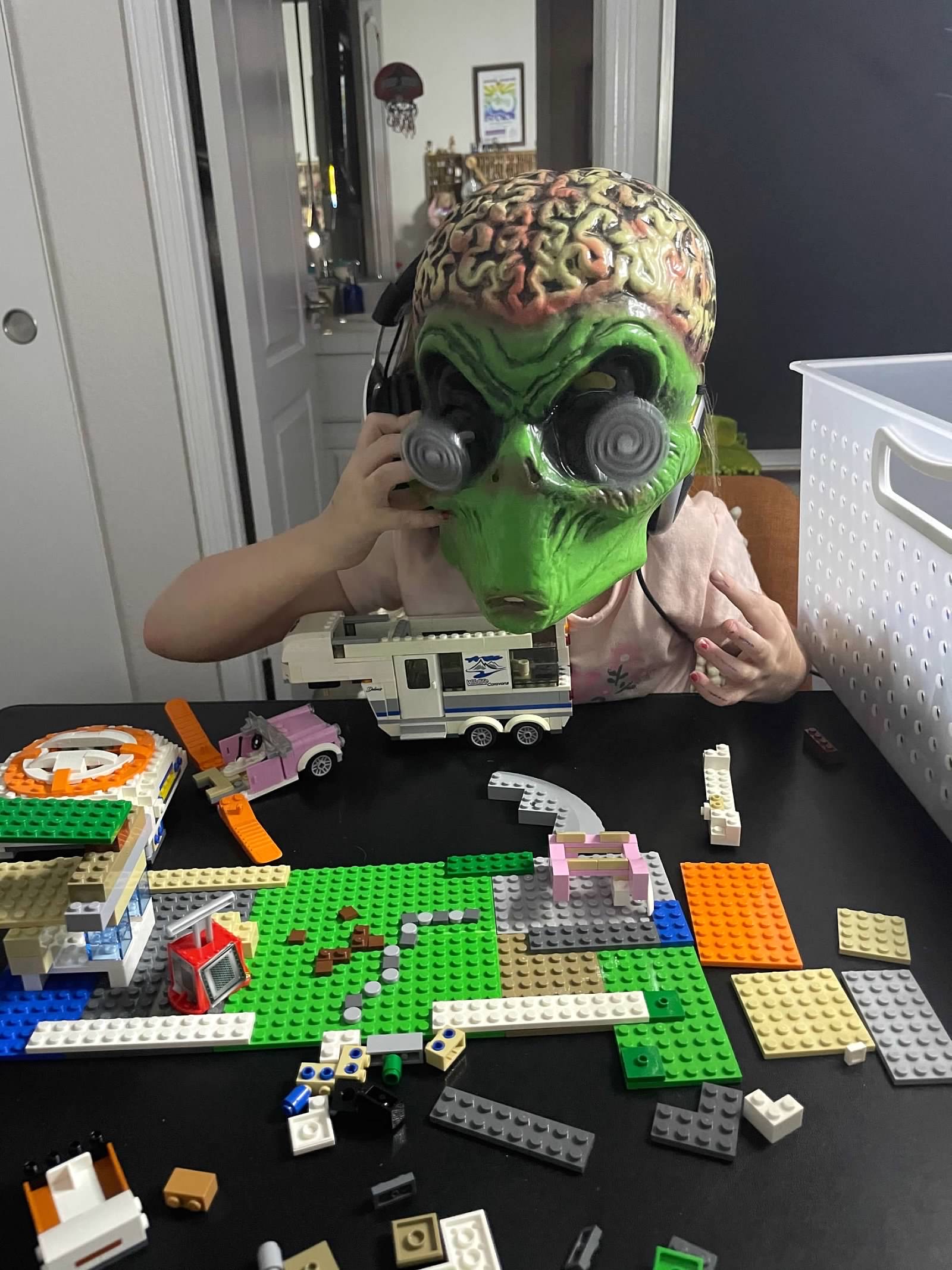 Child wearing alien brain mask doing LEGOs with headphones