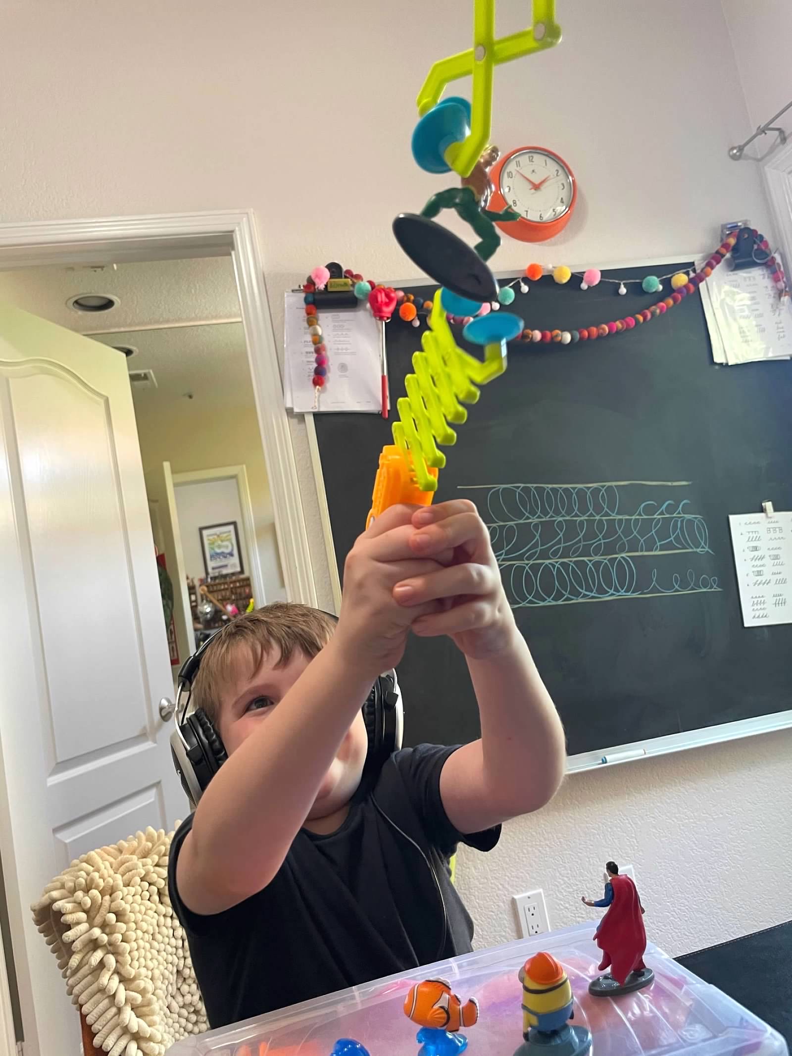 Boy with headphones building colorful toy tower with chalkboard behind