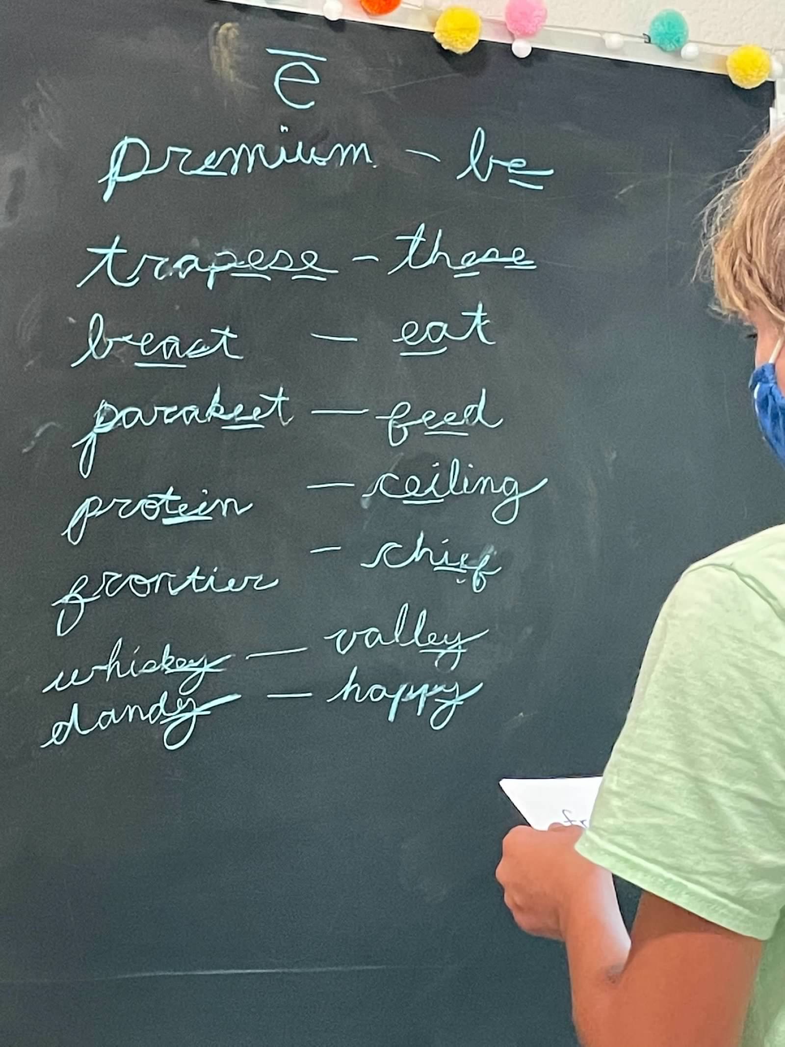 Student writing cursive vocabulary at chalkboard
